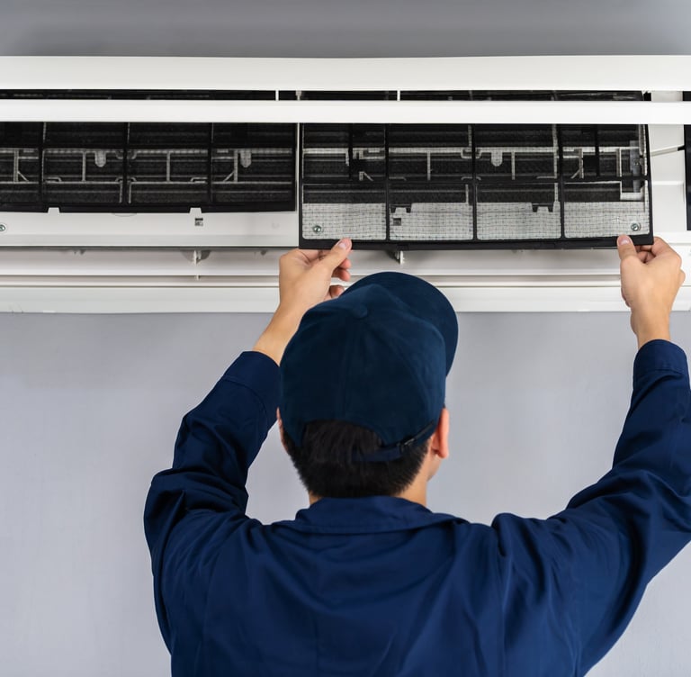 A technician servicing an air conditioner, removing the air filter for cleaning and maintenance purposes.