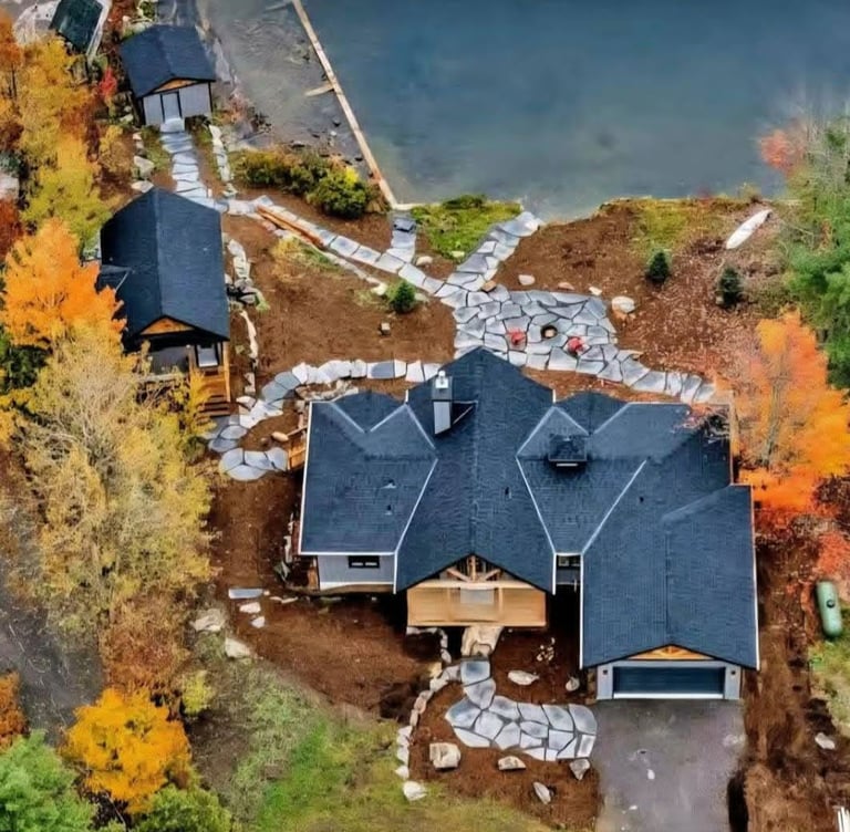 Aerial view of a luxury lakeside cottage with stone walkways and autumn foliage.