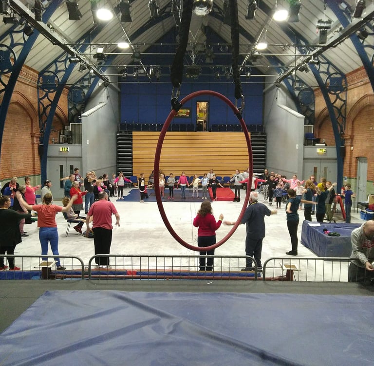 Students practicing aerial arts and circus skills in a large training hall with a red hoop.