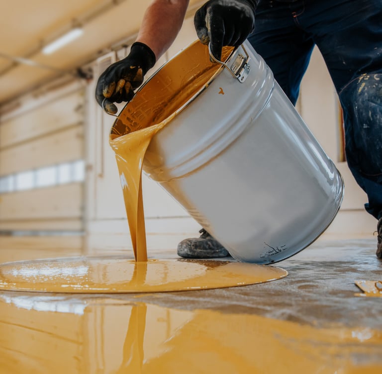 a man is pouring a bucket of paint onto a floor