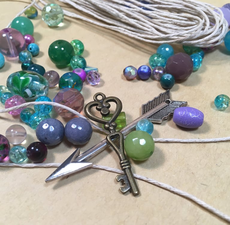 blue, purple, and green beads with key and arrow charm and hemp cord on table