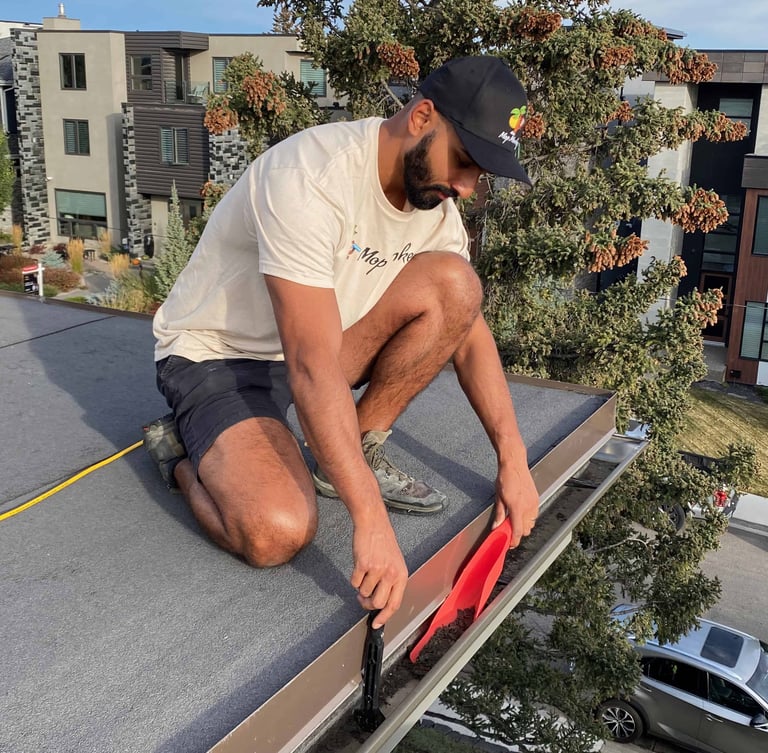Mop Monkey technician cleaning gutters in Calgary from roof with specialty tools