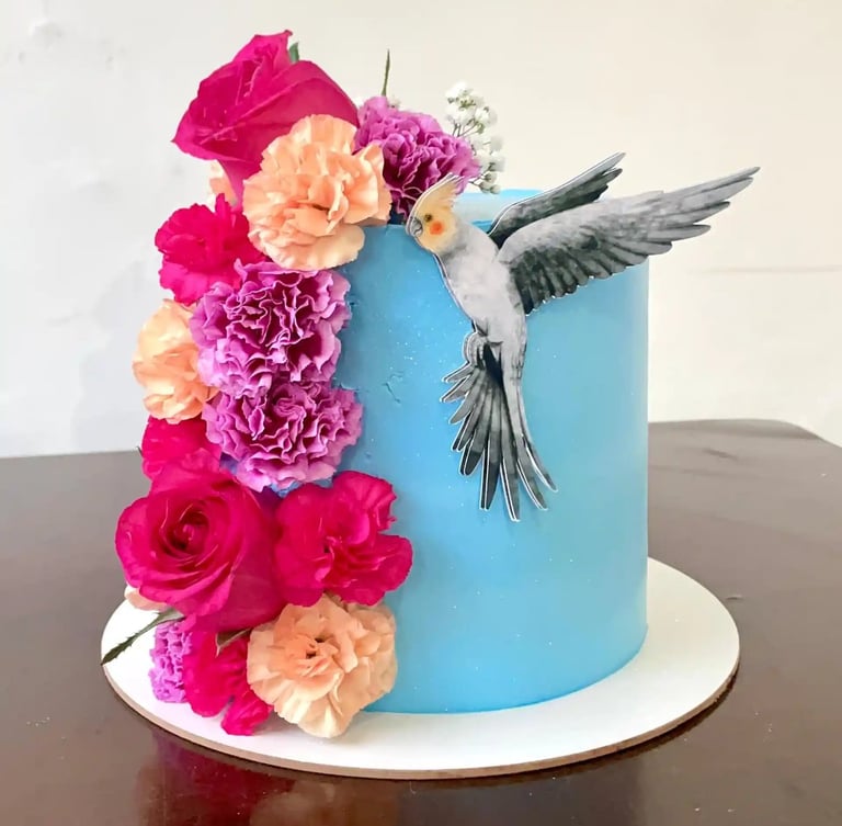 Bolo decorado em azul com flores coloridas e um desenho de um pássaro. Ideal para festas e celebraçõ