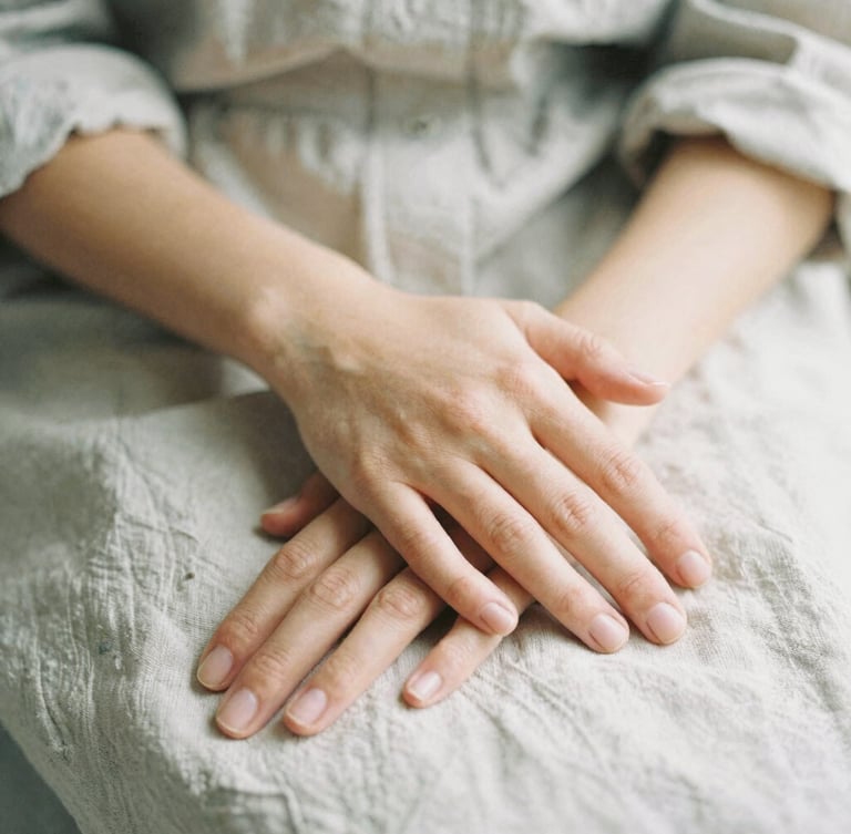 Close-up of gentle hands resting calmly over a linen shirt, soft natural light, shallow depth of field, organic and warm atmosphere