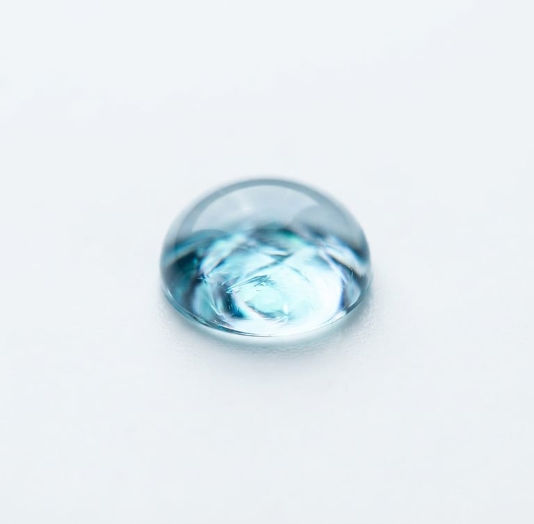Extreme macro photograph of a sterile, clear hydrogel droplet on a pure white surface, light refracting with cool blue and teal undertones, sharp clinical focus, 85mm lens.