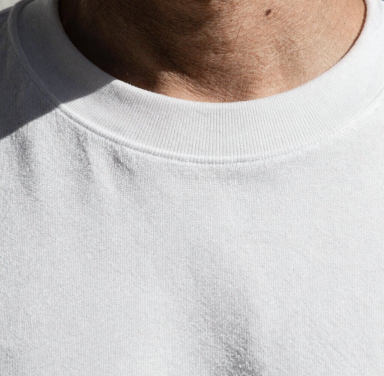 Extreme close-up of a thick ribbed collar and dense cotton weave of a white t-shirt, high-contrast desaturated tone, sharp shadows, raw industrial texture.