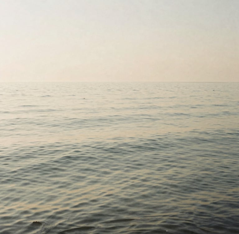 Wide-angle minimalist film photography of still water with gentle ripples at sunrise, soft diffused morning light, desaturated warm sand and sage tones, quiet contemplative mood.