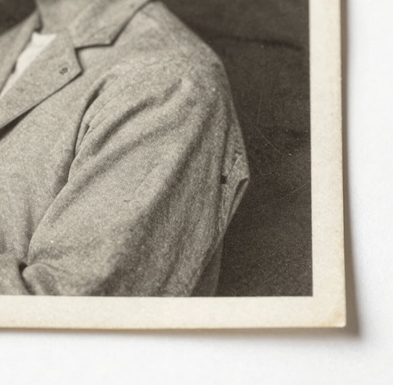 Macro photograph of a vintage 1940s black and white photograph edge, showing silver halide emulsion texture and paper fibers under soft side-lighting, archival museum style.