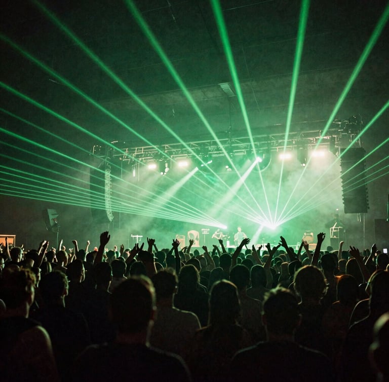 Wide angle shot of a massive concert crowd in Bedford, hands in the air, silhouetted against brilliant green laser lights and heavy stage haze.