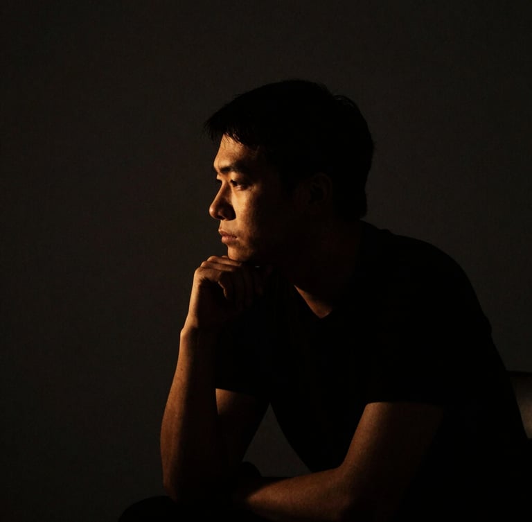 Low-key dramatic portrait of a focused thinker in deep shadow, golden side lighting, minimalist dark background, dark editorial photography, 35mm