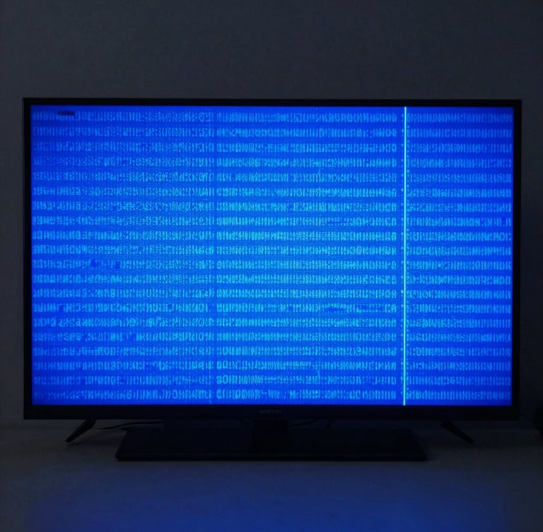 Straight-on shot of a modern television screen displaying a vibrant blue diagnostic test pattern in a clean, high-tech workshop environment.