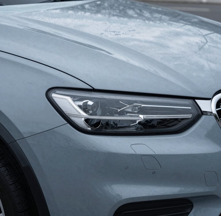 Close-up detail of a modern vehicle headlight and fender, overcast New England daylight, cool slate gray tones, sharp architectural framing