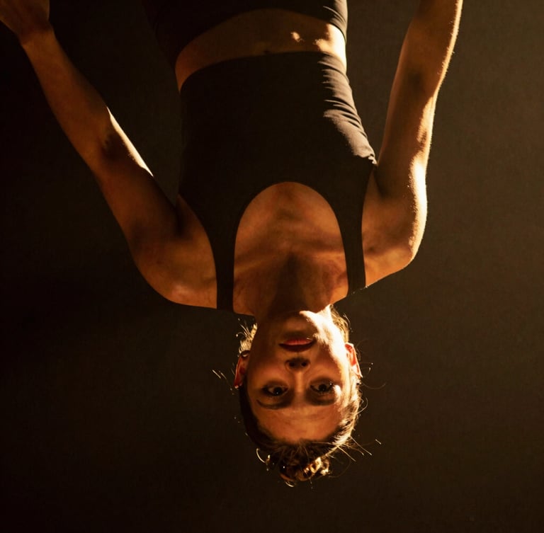 Dramatic close-up of a female aerial hoop artist suspended in mid-air, intense focus on her face, warm golden spotlighting, deep shadows, 35mm cinematic photography.