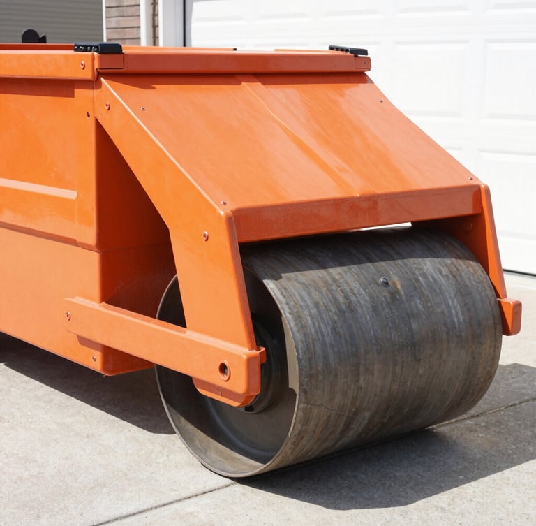Close-up of heavy-duty steel rollers on a roll-off dumpster, showing the mechanism designed to protect driveways, bright midday sun, crisp industrial photography, orange and charcoal tones, sharp focus.