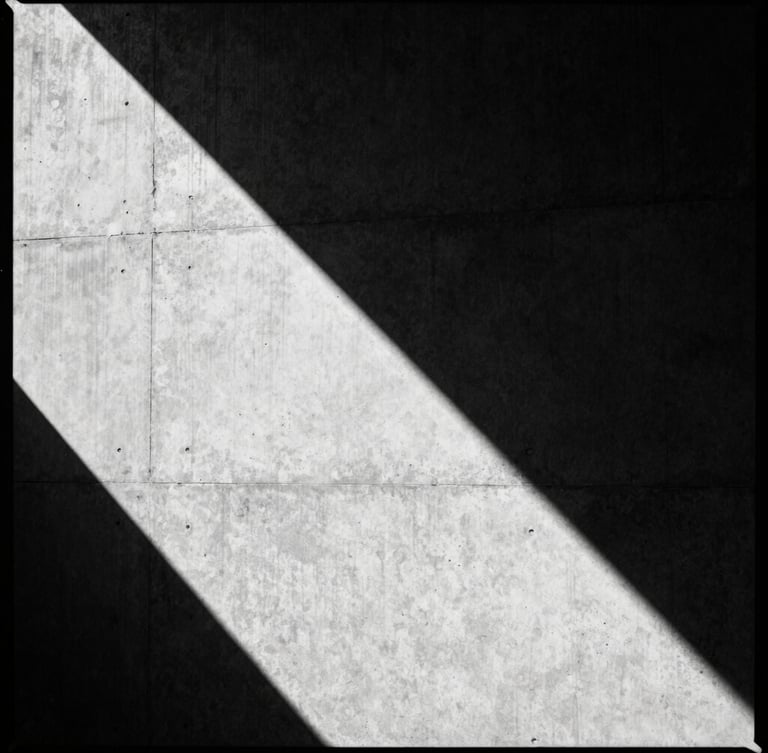 stark editorial fashion photography of a brutalist concrete wall casting sharp geometric shadows, high-contrast monochrome, 35mm film