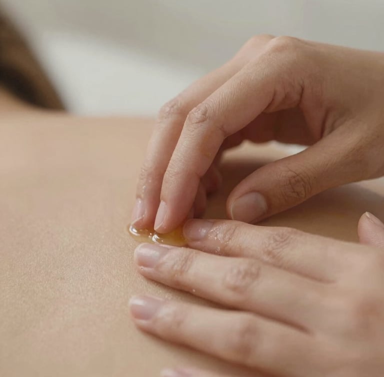 Macro detail of a practitioner's hands gently applying custom-blended botanical oil to skin, soft diffused north-facing daylight, warm sand tones, shallow depth of field, 35mm editorial photography.