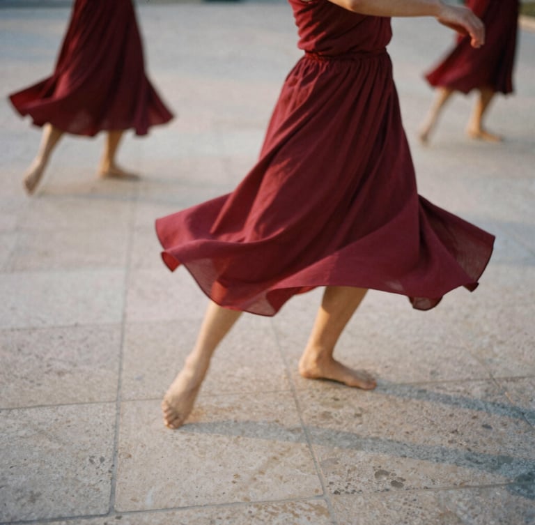 Moody 35mm film photograph of dancers in motion blur on a textured stone plaza, warm natural sunset light, deep cherry red fabrics flowing, organic and raw atmosphere