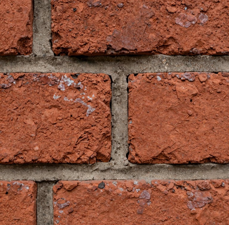 Macro detail of weathered historic red brickwork with deeply recessed mortar joints, natural overcast daylight emphasizing the rough clay texture, sharp focus on central brick edge.