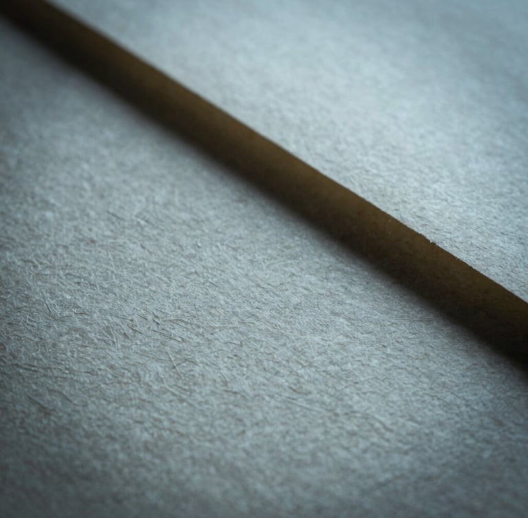 A close-up macro shot of heavily textured handmade paper catching soft, cool raking light, casting deep shadows