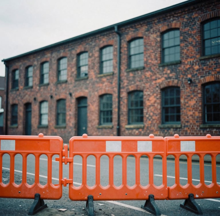 Gritty editorial photo of Salford brick industrial architecture, natural overcast daylight, desaturated cool tones with a sharp orange safety barrier in the foreground, 35mm film grain.
