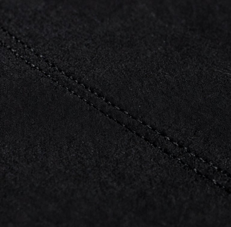 Macro close-up of heavy black cotton fabric texture, detailed stitching, soft moody studio lighting, high contrast monochrome, 35mm