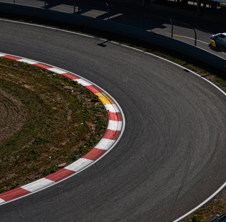 Dramatic top-down aerial shot of a racetrack's sharp asphalt curves, harsh midday sun casting sharp shadows, high-contrast industrial composition.