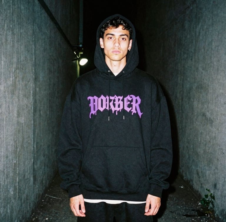 Gritty urban fashion photography, portrait of a young man wearing an oversized black streetwear hoodie with neon purple graphic print, standing in a dark concrete alley, high contrast, 35mm film grain