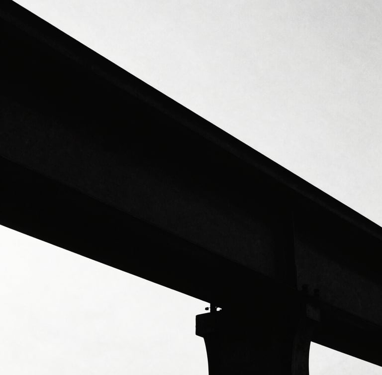 Stark high-contrast silhouette of a structural steel beam against a blinding white sky, deep black shadows, minimalist composition, raw texture, 35mm film grain