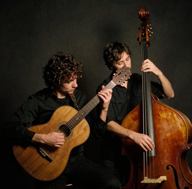 Low-key atmospheric portrait of two musicians holding a vintage steel resonator guitar and upright bass, warm side lighting, dark charcoal background, 35mm film grain