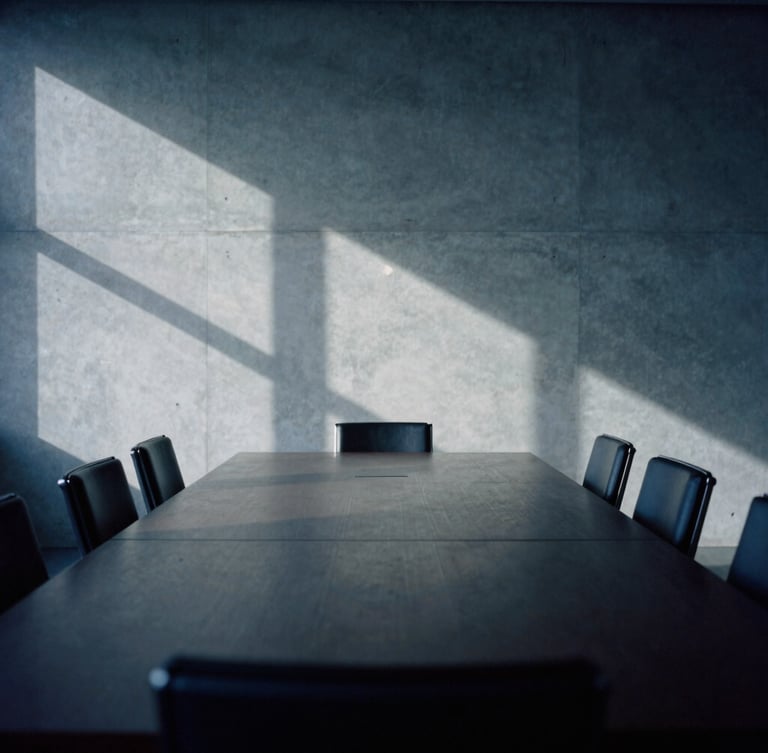 An empty high-end boardroom in Luxembourg City, soft natural northern light casting abstract geometric shadows on a concrete wall, minimalist composition