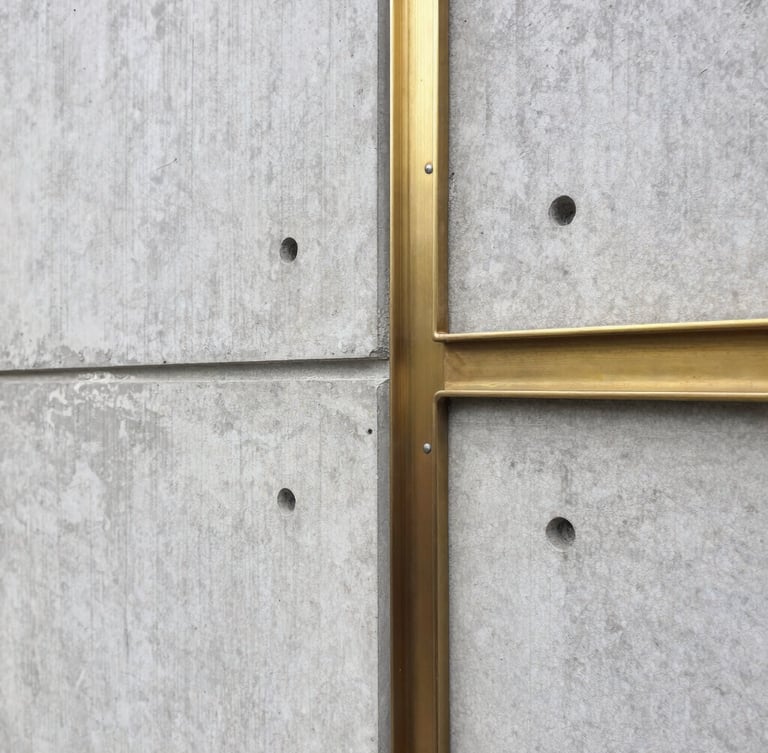 Sober architectural photography of a raw concrete wall meeting a brushed brass structural joint, natural diffused daylight, sharp focus