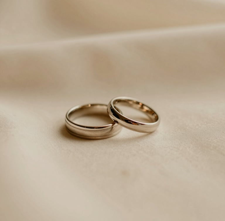 Close-up of elegant wedding rings resting on a soft cream fabric, warm diffused golden light, shallow depth of field, serene editorial photography