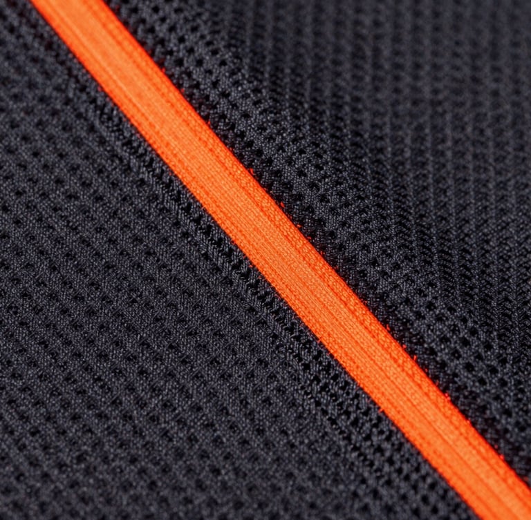 Macro photograph of high-contrast athletic fabric weave, sharp neon-orange stitching detail, dark charcoal technical mesh background, professional studio lighting, 85mm lens