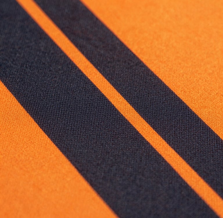 Close-up of vibrant sublimated soccer jersey fabric, deep charcoal and neon-orange patterns, sharp focus on technical fiber pores, bright studio lighting, 85mm lens