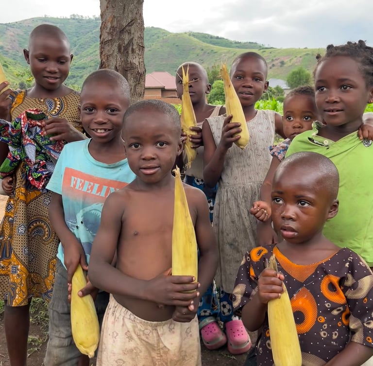 A group of smiling African children holding fresh ears of corn in a rural village setting.