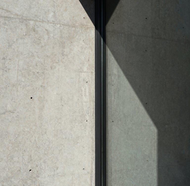 Extreme close-up of a raw concrete wall meeting a clean glass panel, sharp natural light casting a geometric shadow, architectural detail, desaturated, 35mm