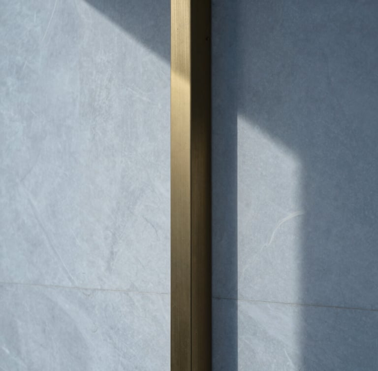 Extreme close-up of a polished white Swiss quartzite wall meeting a brushed brass column, sharp geometric shadow lines, cool overcast morning light, 35mm.