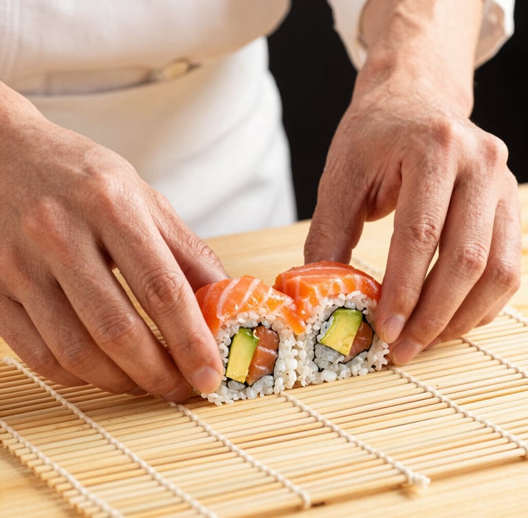 Close-up of a chef's hands carefully rolling a sushi roll with fresh avocado and salmon, clean bamboo mat, warm directional studio light, premium feel
