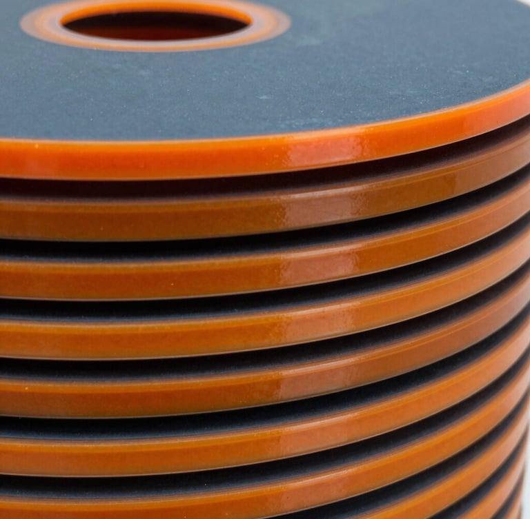 Macro shot of freshly cured polyurethane sealing discs stacked in an Indonesian engineering facility, crisp high-contrast lighting highlighting the glossy orange elastomer edges.