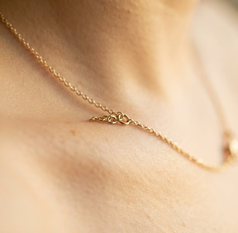 Extreme macro close-up of a delicate tarnish-resistant gold necklace catching soft golden-hour window light on warm skin, shallow depth of field, minimalist editorial style