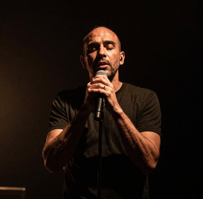 Dramatic stage lighting on Pierre-Yves Clarence performing live, low-key photography, deep shadows, high contrast, warm amber undertones, vertical portrait crop
