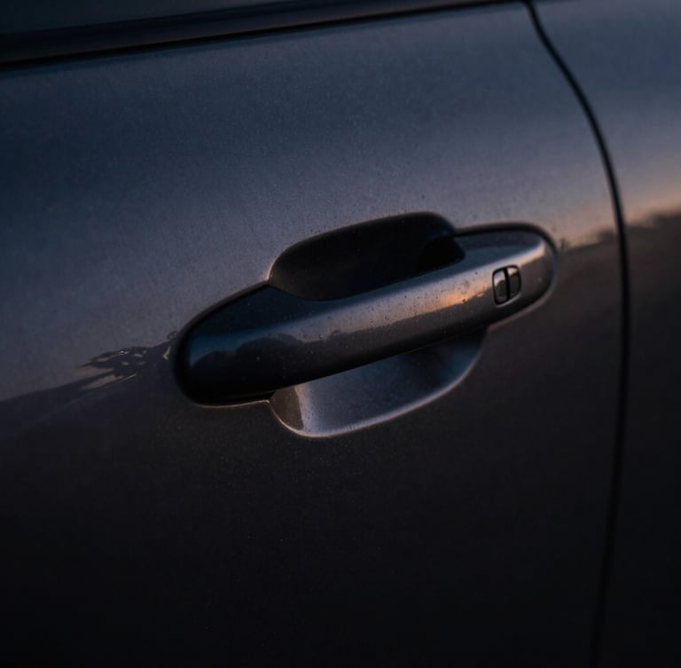 Extreme close-up of a dark brushed metal vehicle door handle, dramatic single-source shadow, cool twilight ambient light, high-contrast.