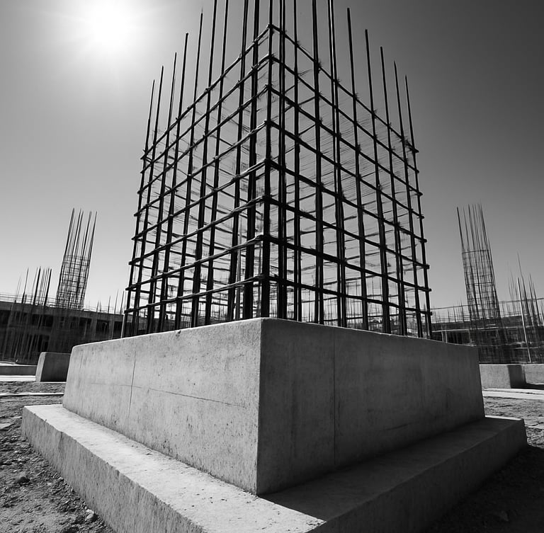 Low-angle architectural shot of a reinforced concrete foundation footing on an active construction site in Bareilly, steel rebar grid visible, harsh midday sun, high-contrast concrete tones