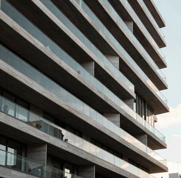 Vista arquitectónica abstracta de un edificio residencial moderno de hormigón y vidrio en Madrid, líneas geométricas limpias, luz natural difusa de la mañana, encuadre simétrico de ángulo contrapicado.