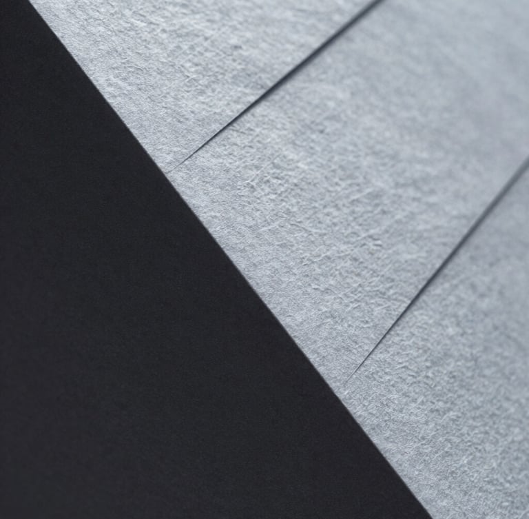 Macro close-up of high-texture heavy cotton paper with blind debossed geometric lines, sharp side-lighting, silver-gray shadows, minimalist architectural feel.