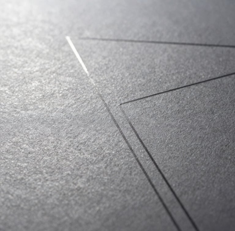 Macro close-up of fine-textured heavy cotton paper with a subtle debossed geometric line, dramatic side-lighting, silver and charcoal tones, sharp focus.