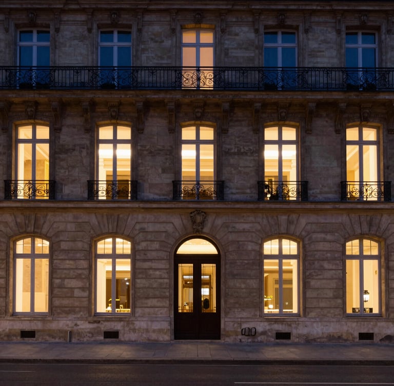 Symmetrical wide shot of a classic Parisian stone building facade with warm interior window lights at dusk, clean architectural lines, deep shadows, 35mm lens