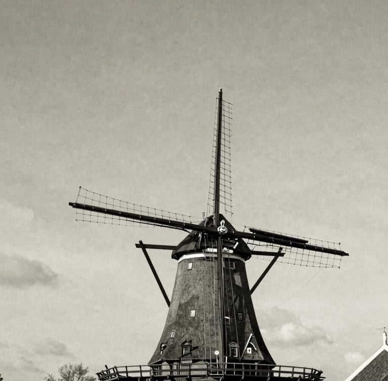 Historic black and white photograph of Molen De Lelie in the Dutch landscape, majestic sails angled against a soft textured sky, vintage editorial style