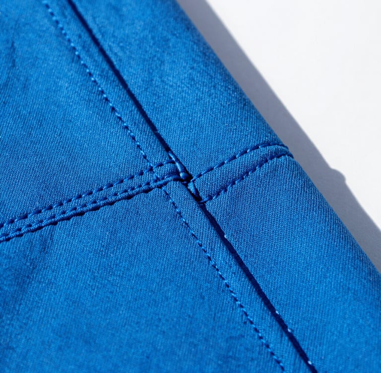 Close-up macro shot of durable double-stitched seams on vibrant electric blue canvas fabric, bright natural sunlight, crisp shadows, 35mm