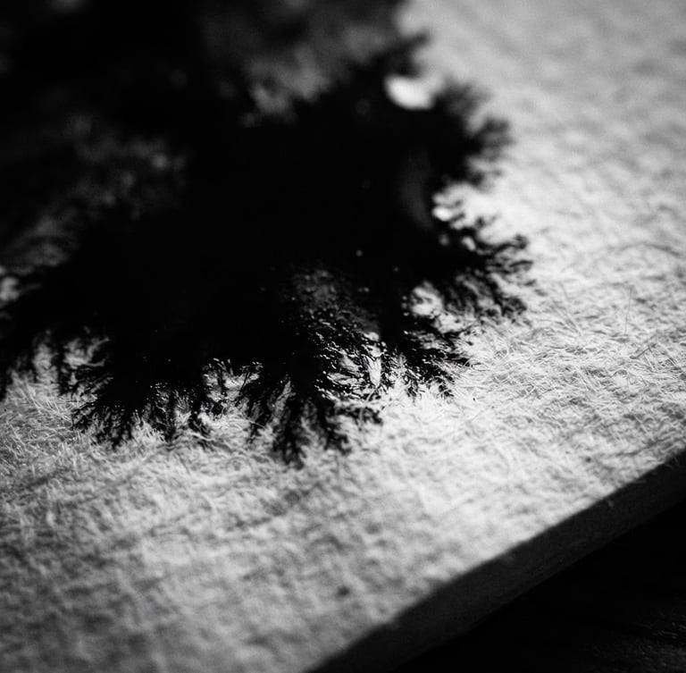 Stark black and white photography, macro shot of black ink bleeding slowly into thick textured white paper, high-contrast chiaroscuro lighting, deep shadows, 35mm film grain.